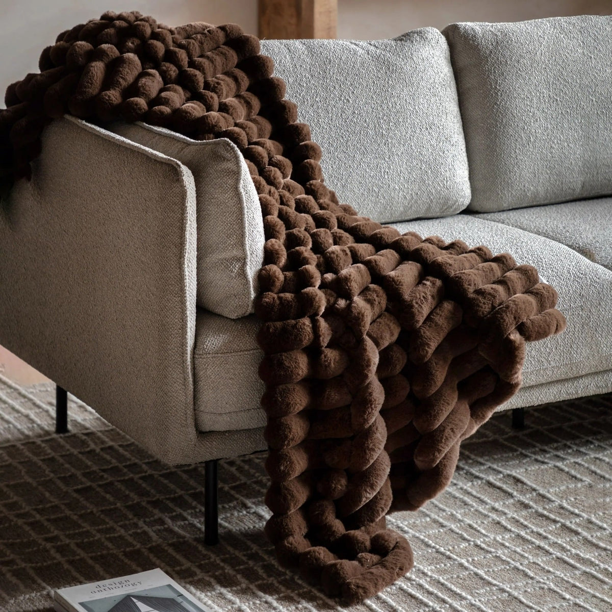 Brown faux fur throw with textured design draped over grey modern sofa in a living room.