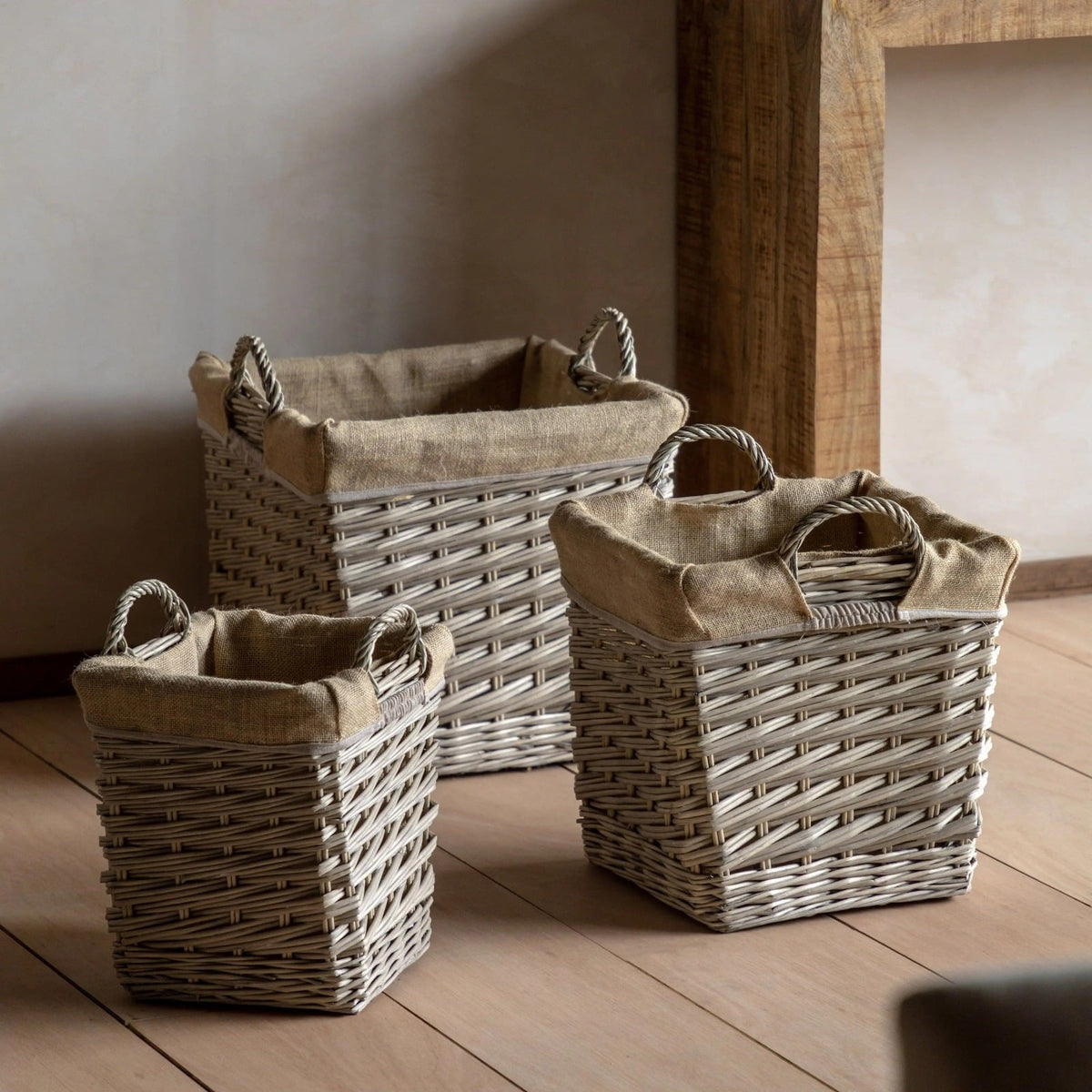 Three woven storage baskets with natural fabric lining, styled in a rustic interior setting on wooden flooring.