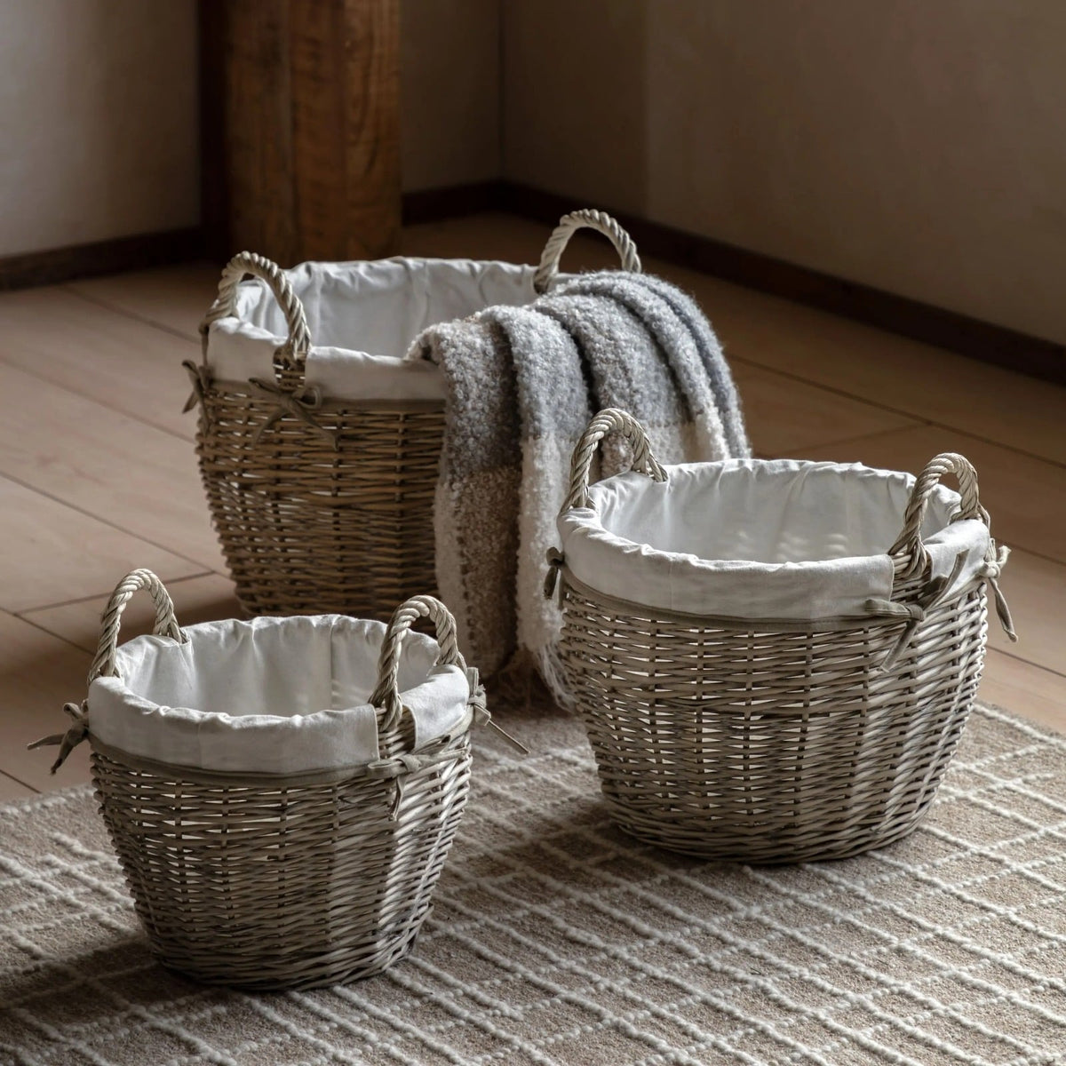 Set of three wicker storage baskets with fabric liners, styled on a rug with a grey throw blanket for rustic home décor.