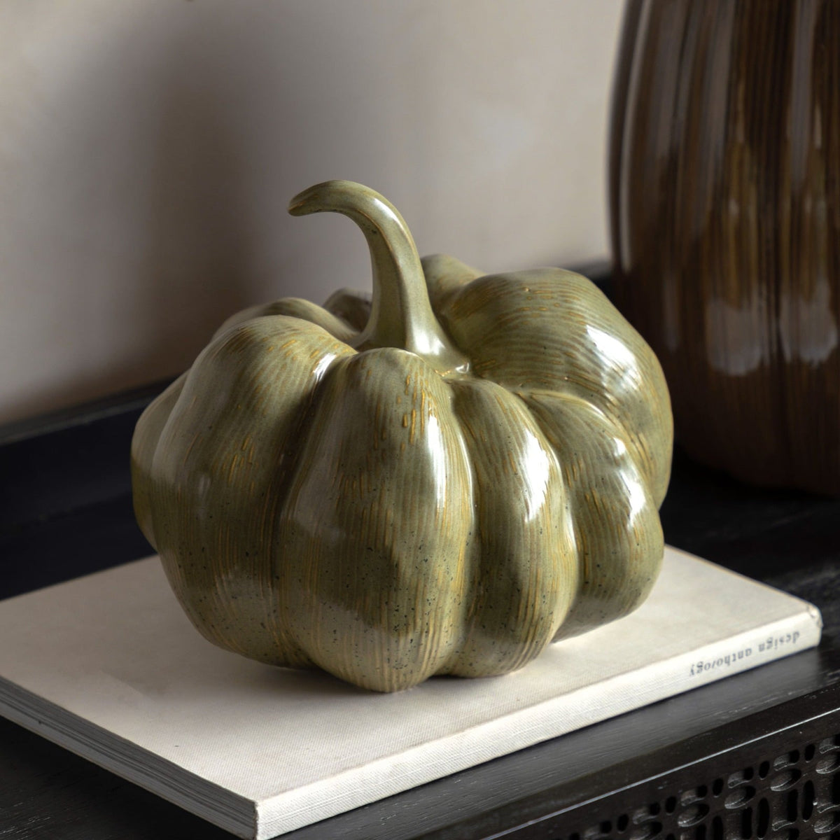 Green ceramic pumpkin ornament styled on a book for autumn home décor.