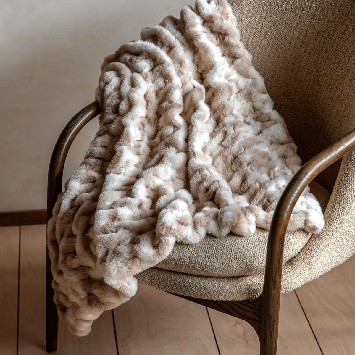 Plush beige and ivory faux fur throw blanket draped over armchair, cosy textured accent for modern home interiors.