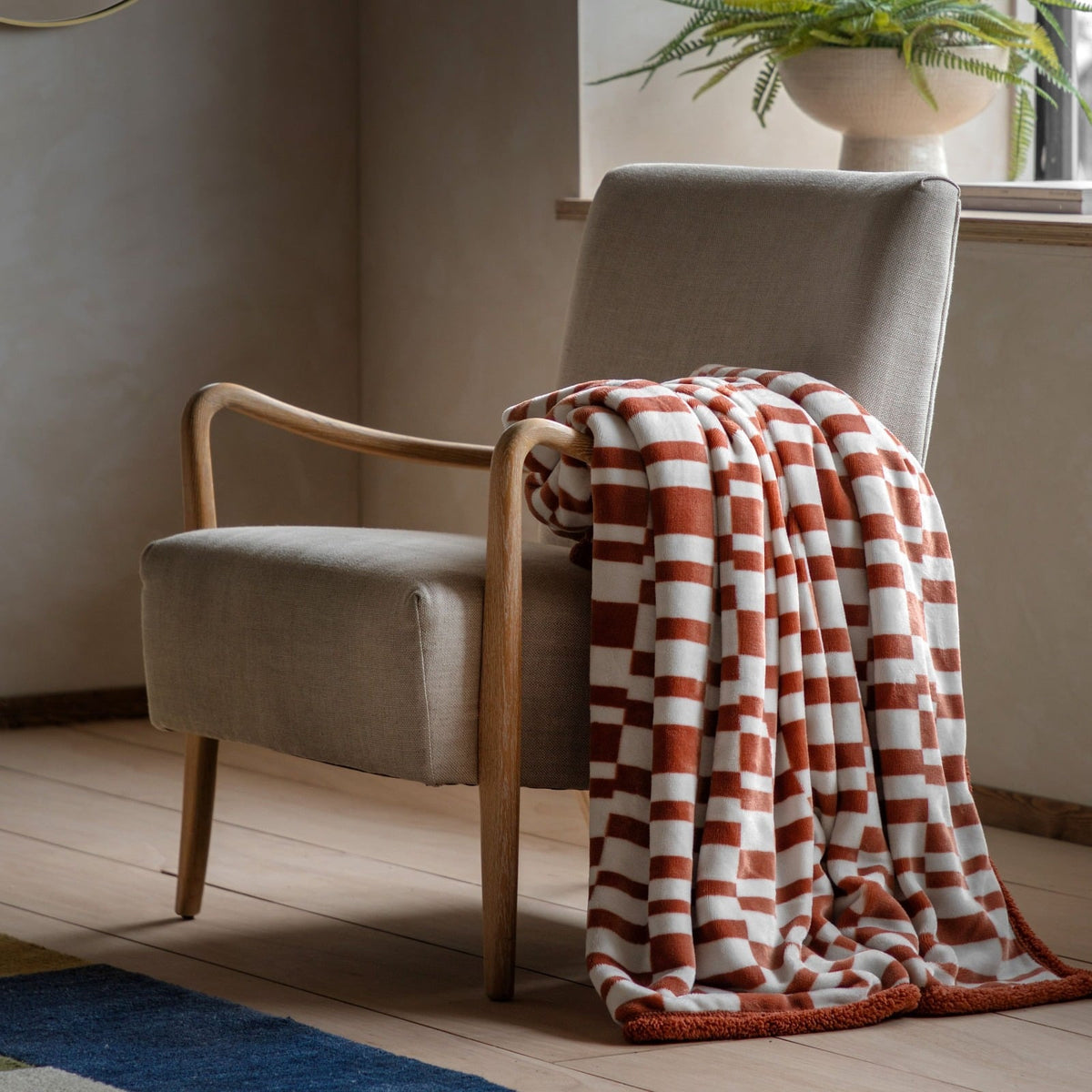 Soft geometric patterned throw blanket in rust and cream draped over a modern wooden armchair in a cosy living room setting.