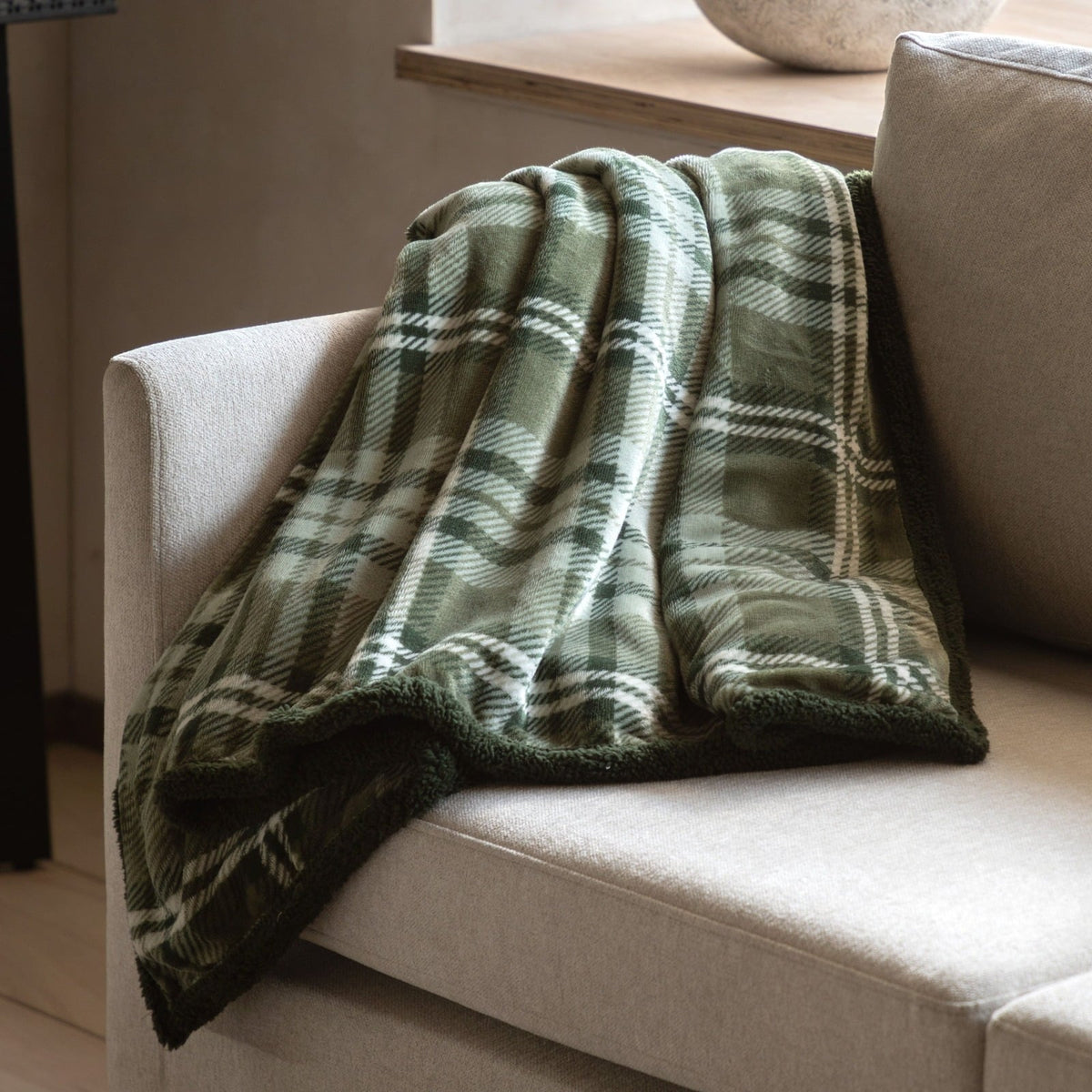 Green plaid fleece throw casually displayed over light grey couch.