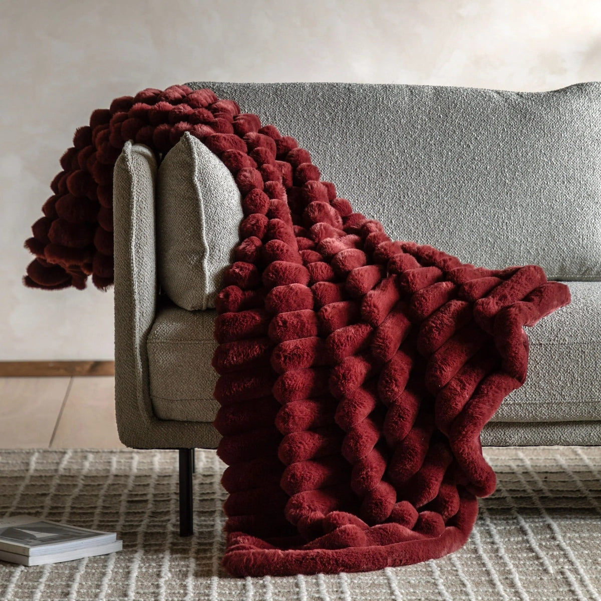Luxurious deep red faux fur throw blanket draped over a modern grey sofa, adding warmth and texture to contemporary living room decor.
