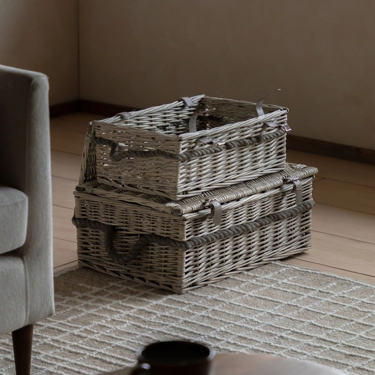 Set of two wicker storage baskets with rope handles and leather straps, styled in a modern living room on a neutral rug.