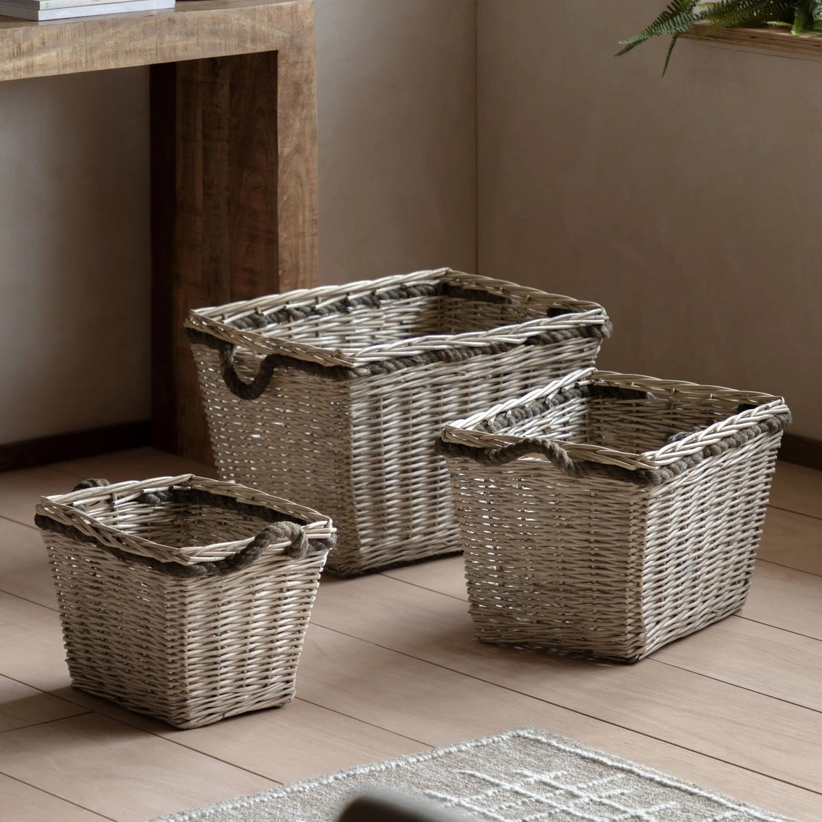 Set of three rectangular wicker storage baskets with rope handles, styled under a wooden console table in a modern living room.