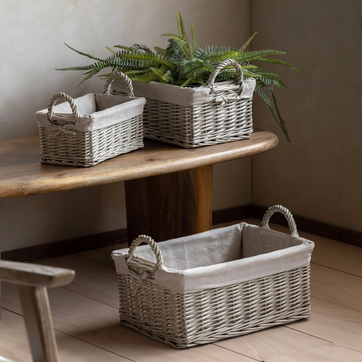 Set of three wicker storage baskets with linen lining, styled with greenery on a wooden table for a rustic home interior look.
